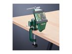 A green table clamp with a circuit board held in its jaws, attached to a wooden table.