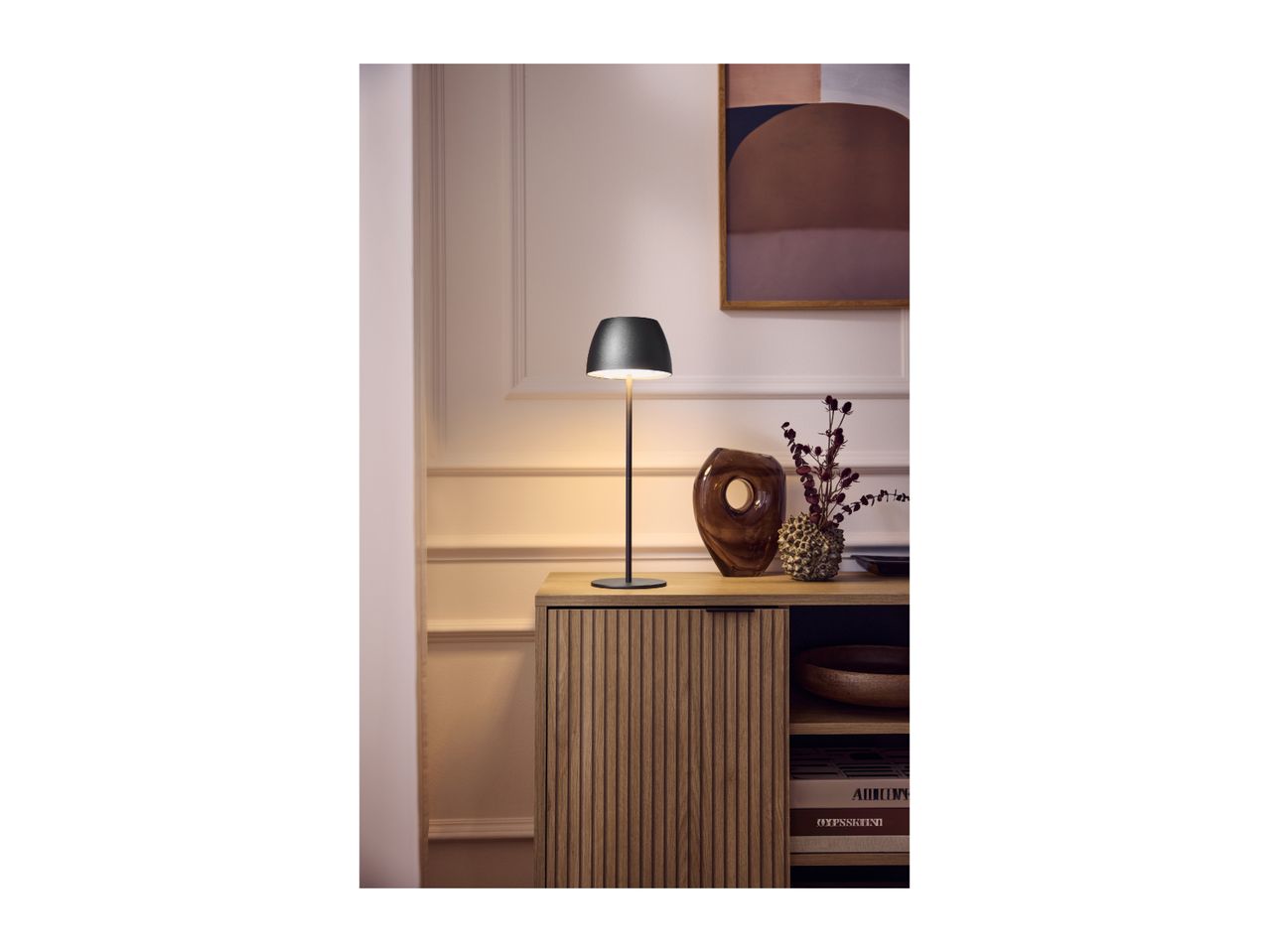 Modern black table lamp on a wooden sideboard with decorative vases.