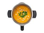 Top-down view of a soup maker filled with orange pumpkin soup, garnished with croutons and parsley.