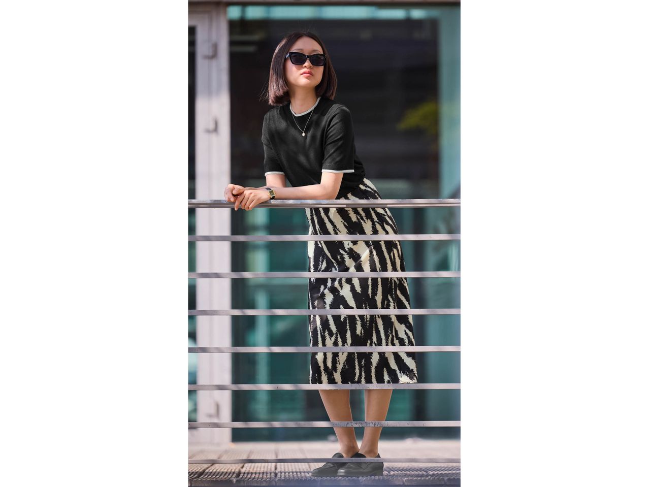 Woman in black top, zebra print skirt, and sunglasses leaning on a railing.