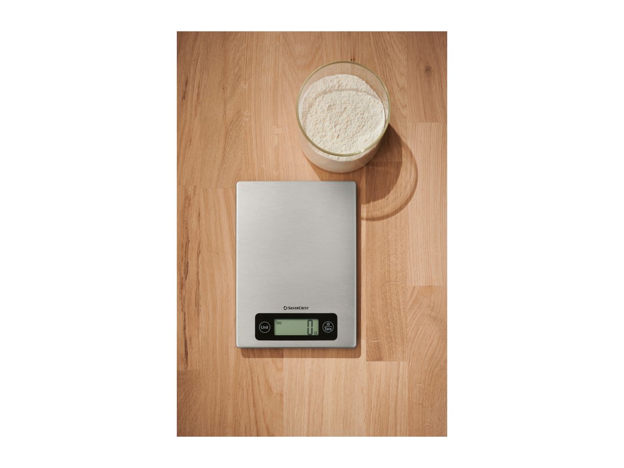 Kitchen scale and a bowl of flour on a wooden surface.