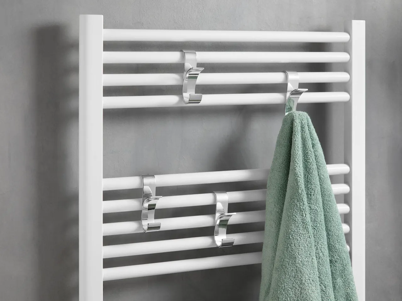 White towel warmer with chrome hooks and a green towel.