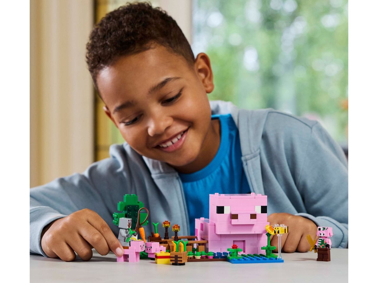 A boy playing with a LEGO Minecraft pig farm set.