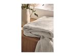 Folded light grey towels on a wooden surface with a white vase and green foliage.