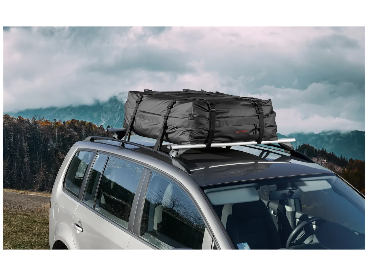 Sac de toit de voiture noir sur un porte-bagages, avec un paysage montagneux en arrière-plan.