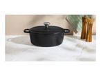Black cast iron Dutch oven with a lid, a green pot holder, and two wooden salt and pepper mills.