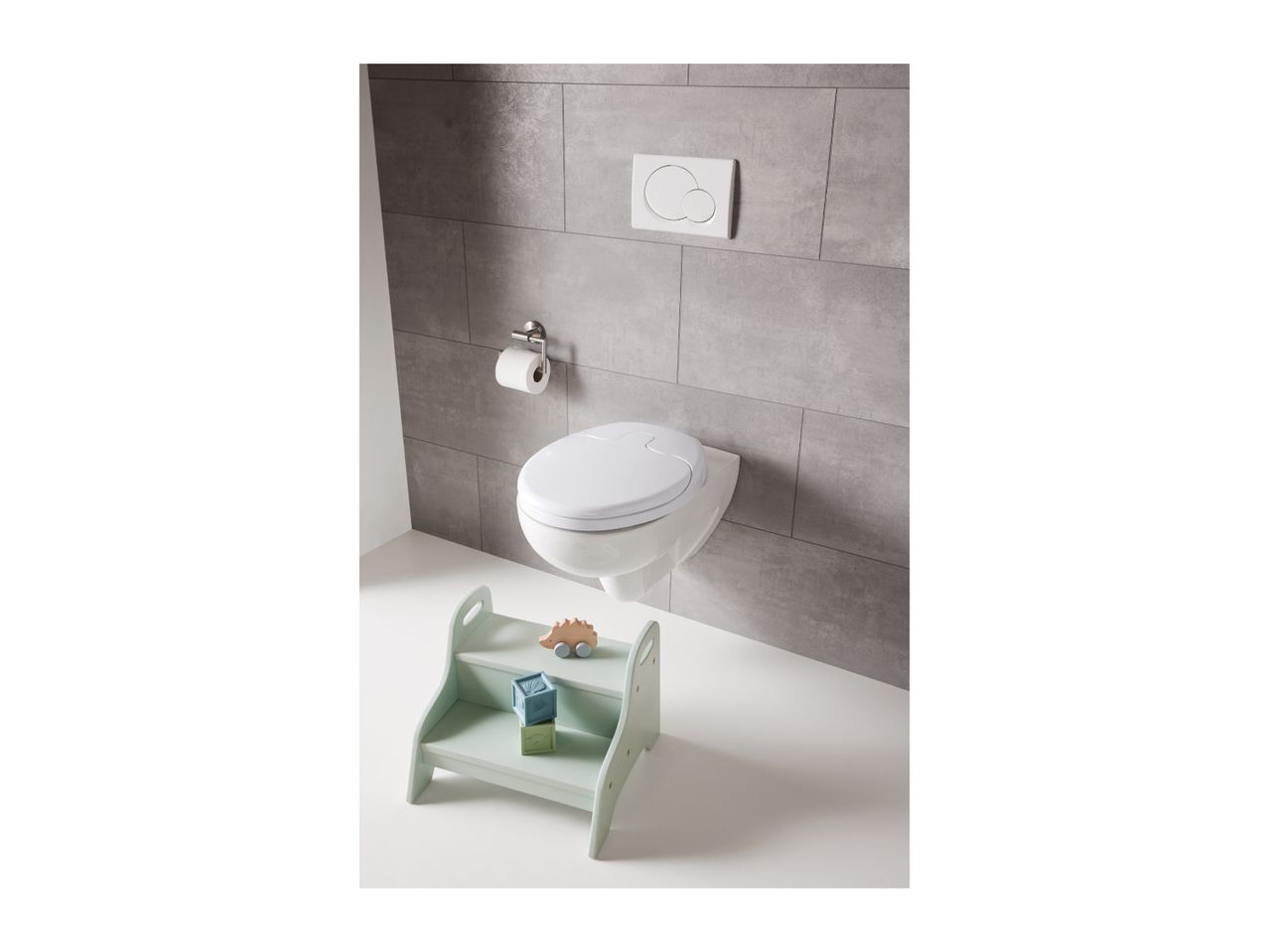Wall-mounted toilet with a child seat, toilet paper holder, and a step stool with toys.