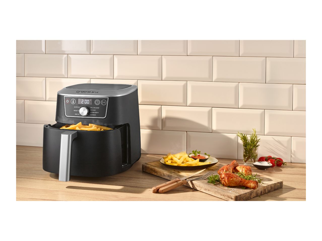 Black air fryer with french fries and chicken drumsticks on a wooden countertop