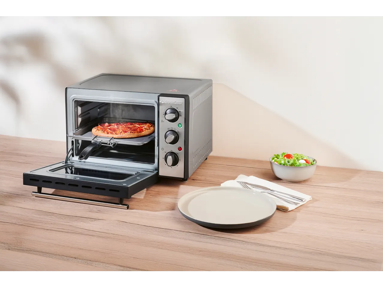 SILVERCREST mala rerna sa picom, tanjirom i salatom na drvenom stolu.