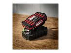 A red and black power tool battery charging on a black charger, on a wooden surface.