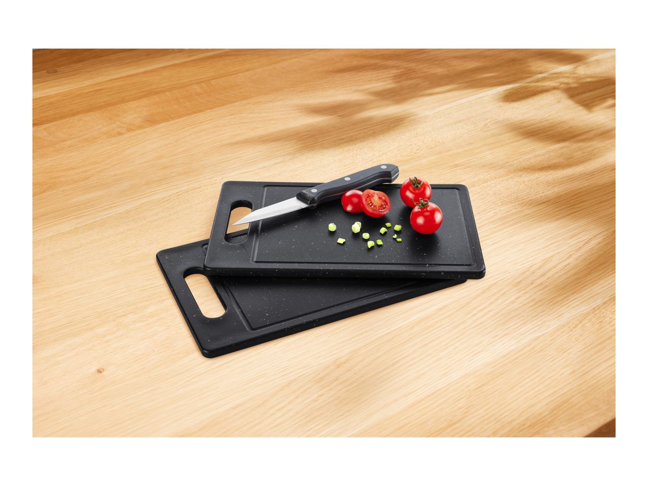 Two black cutting boards with a knife, tomatoes, and chopped chives on a wooden table.