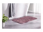 Pink bath mat with a textured pattern on a tiled floor next to a white bathtub.