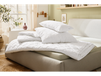 White quilted pillows and duvets stacked on a bed in a bright bedroom.