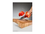 A red bell pepper being sliced in mid-air with a knife above a wooden cutting board.
