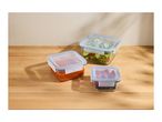 Three glass food storage containers with blue lids, filled with salad, sauce, and berries, on a wooden surface.