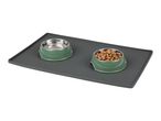 A grey silicone pet feeding mat holds two sage green bowls; one is empty, the other contains dog food.