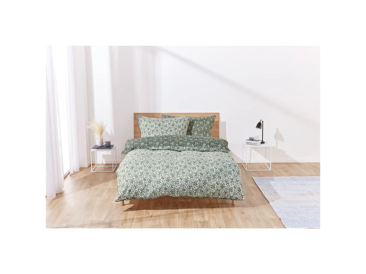 A bed with a teal floral duvet cover and matching pillowcases sits in a bright bedroom.