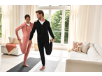 Couple in tracksuits stretching on yoga mats in a bright living room.