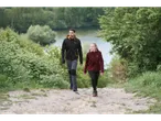 Two people in CRIVIT sports tops walking on a dirt path near a lake.