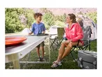 A woman and child camping with a folding table, camping chairs, and tents in the background.