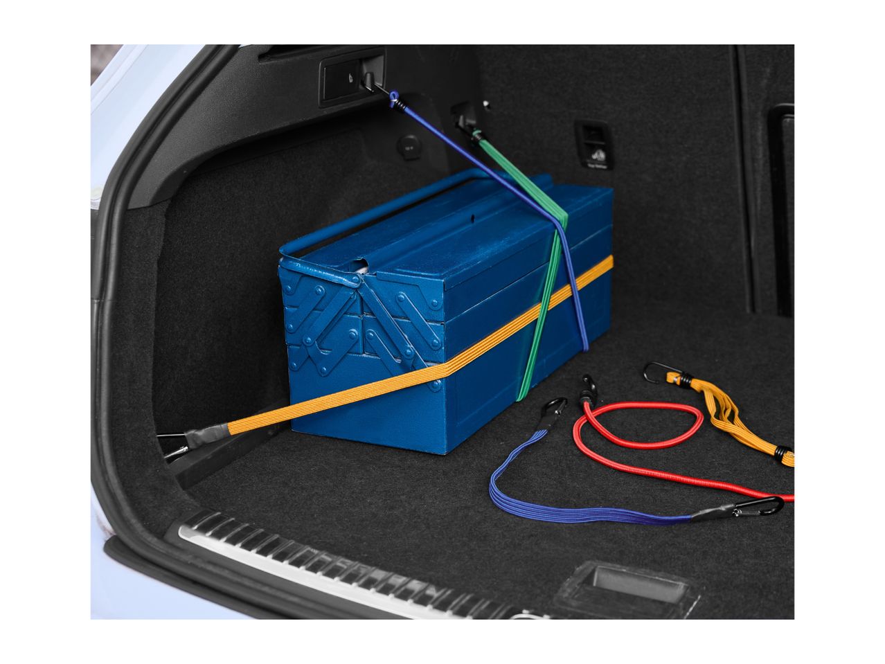Blue toolbox secured with bungee cords in a car trunk, with additional cords on the side.