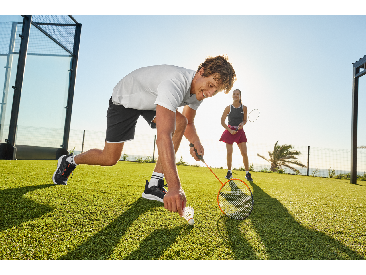 Homem e mulher a jogar badminton com conjunto CRIVIT num campo exterior ensolarado.