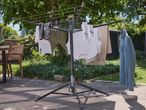 A black rotary clothesline with various clothes drying on a patio.