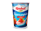 Yoghurtbeker met aardbeien en een lepel roze yoghurt, tegen een bergachtig landschap.