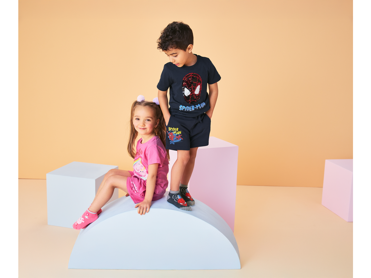 Two children wearing jersey shorts, a boy in Spider-Man shorts and a girl in pink shorts.