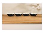 Four black and white bowls on a wooden surface with plant shadows on the wall.
