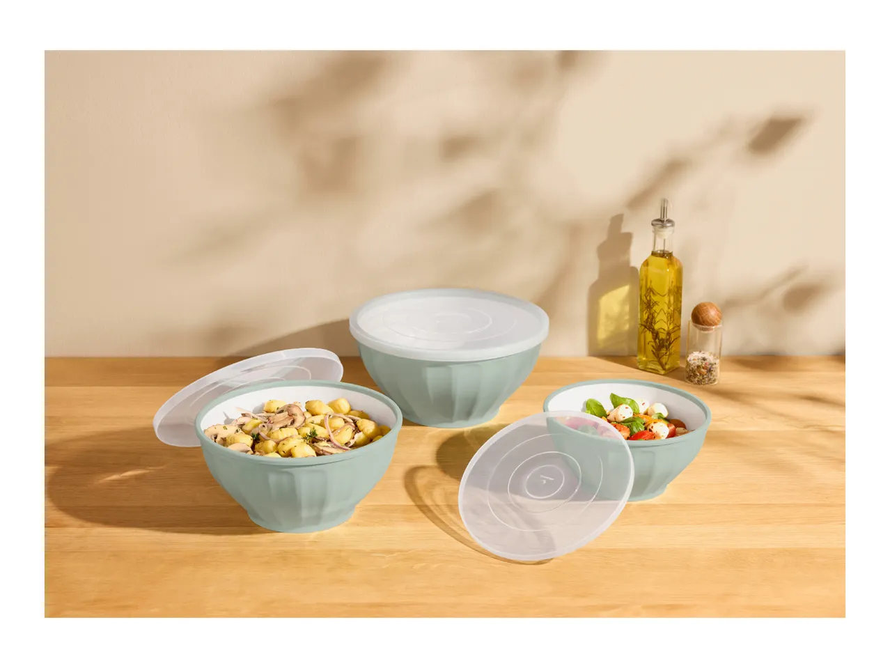 Three light green bowls with lids, two filled with food, on a wooden table.
