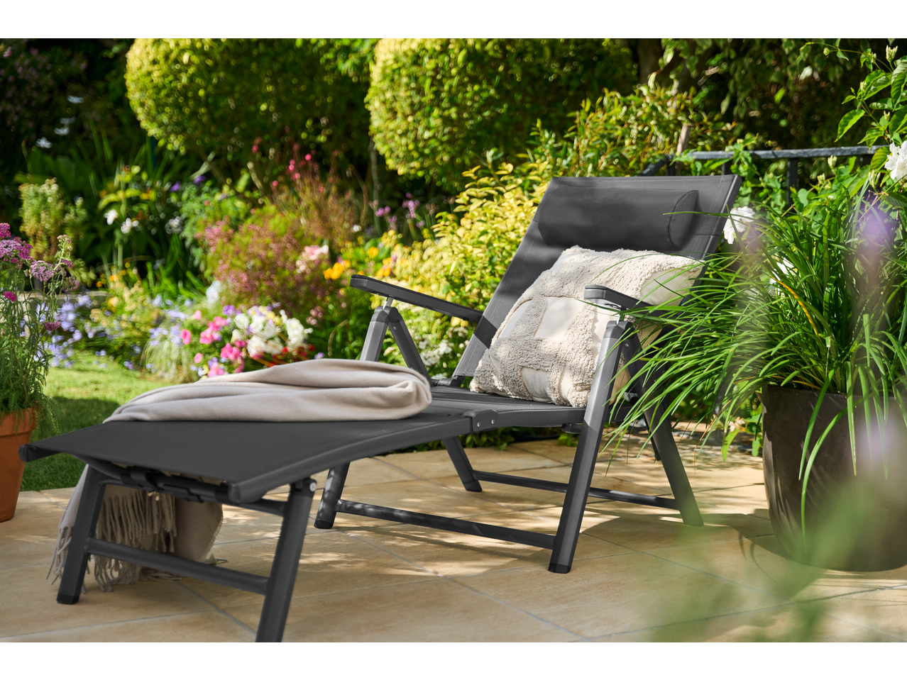 LIVARNO HOME aluminijumska ležaljka sa jastukom i ćebetom u cvetnom vrtu.