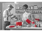 Couple in kitchen with red kitchen appliances, including a kettle.