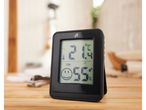 A black digital indoor thermometer and hygrometer sits on a wooden surface.
