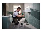 Man using a drain cleaning tool to unclog a sink in a bathroom, with other tools nearby.