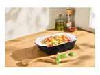 Baked pasta with tomatoes and basil in a black and white rectangular baking dish on a wooden board.