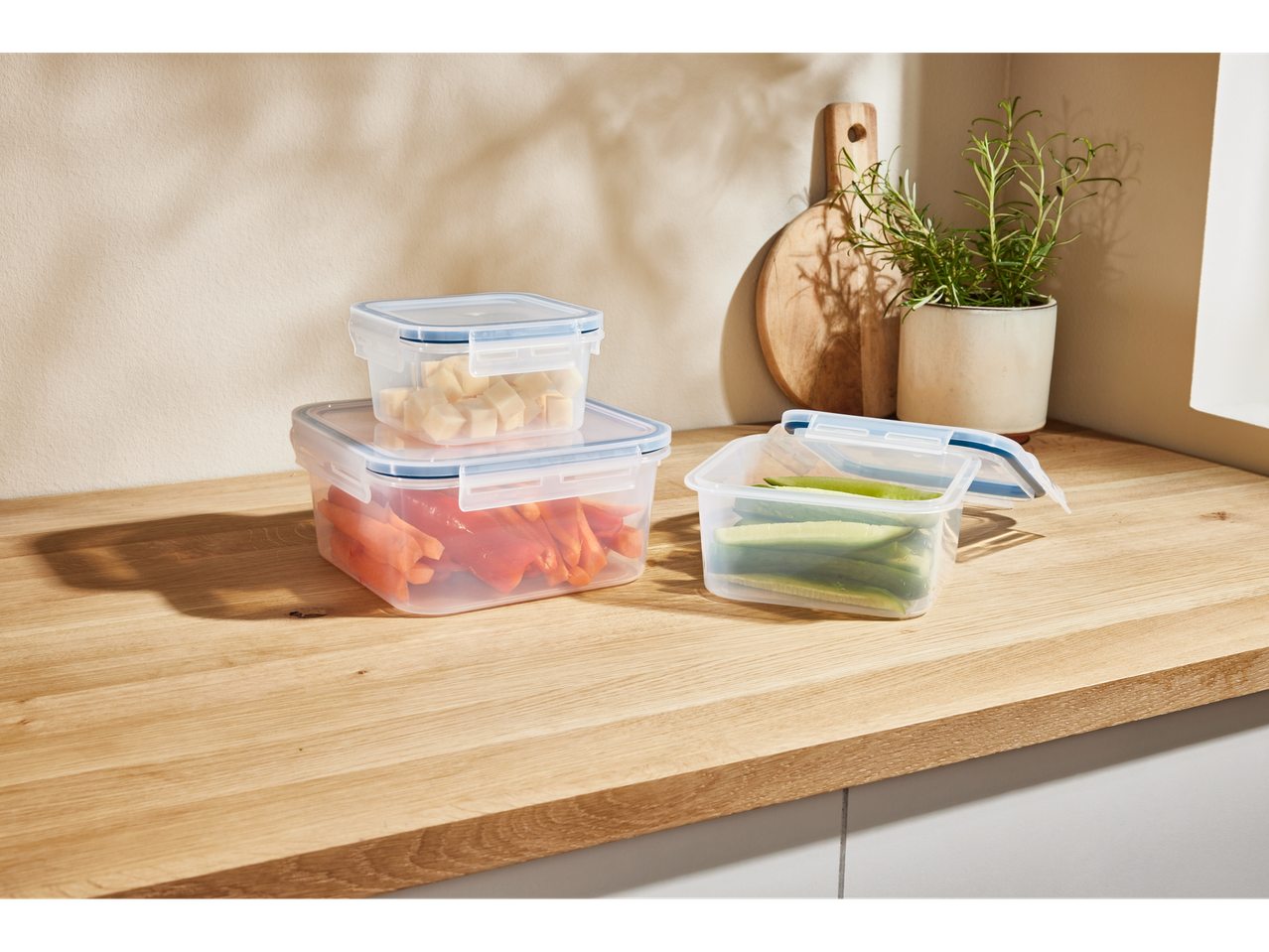 Trei recipiente transparente pentru alimente, cu diverse produse alimentare, pe un blat de lemn.
