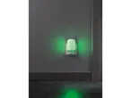 A green night light plugged into a wall socket, illuminating a dark room.
