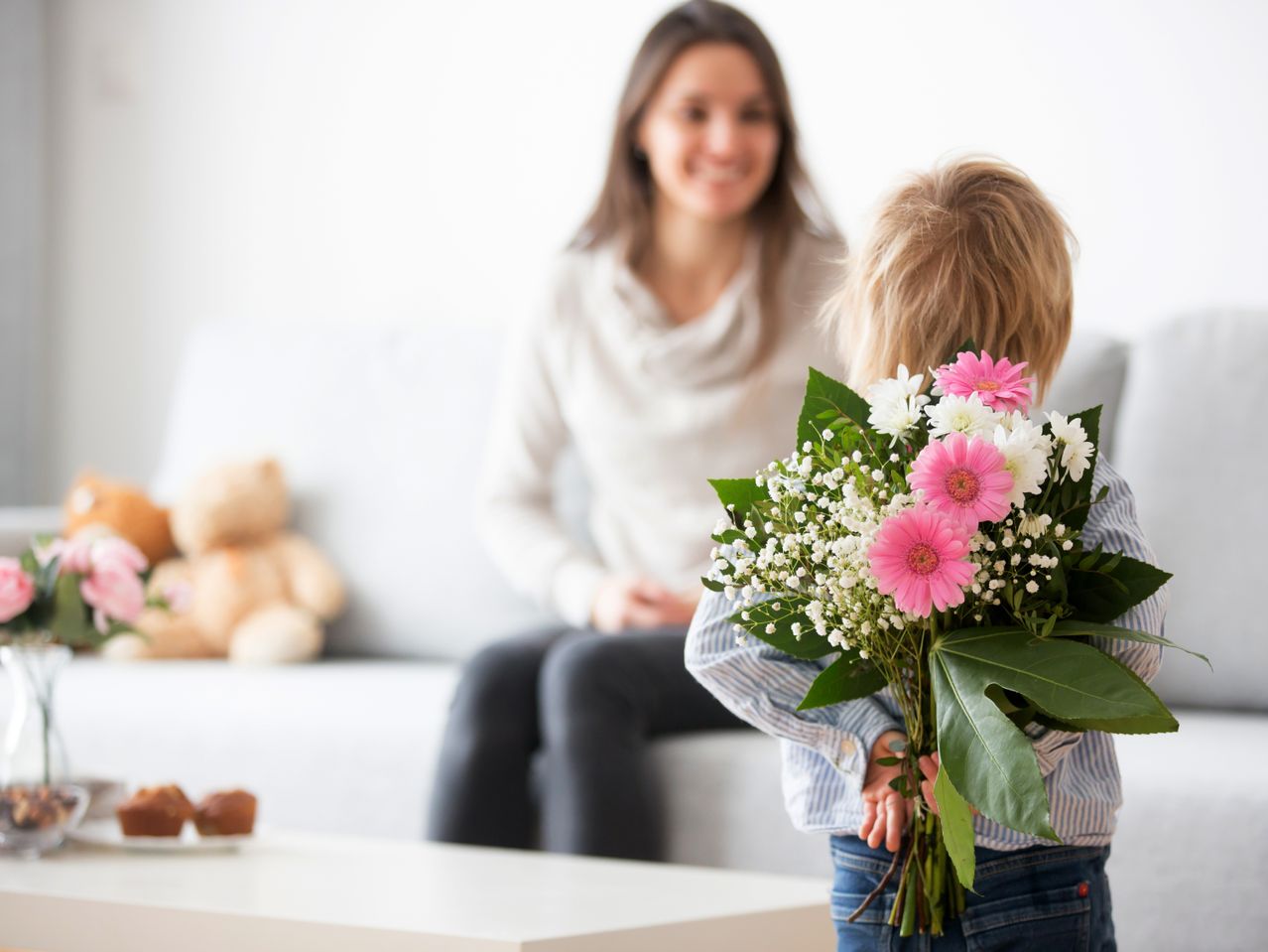 Lille barn holder blomsterbuket bag ryggen til en smilende kvinde.