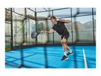 Man in black sportswear playing padel on a blue court, holding a racket, with a ball in the air.