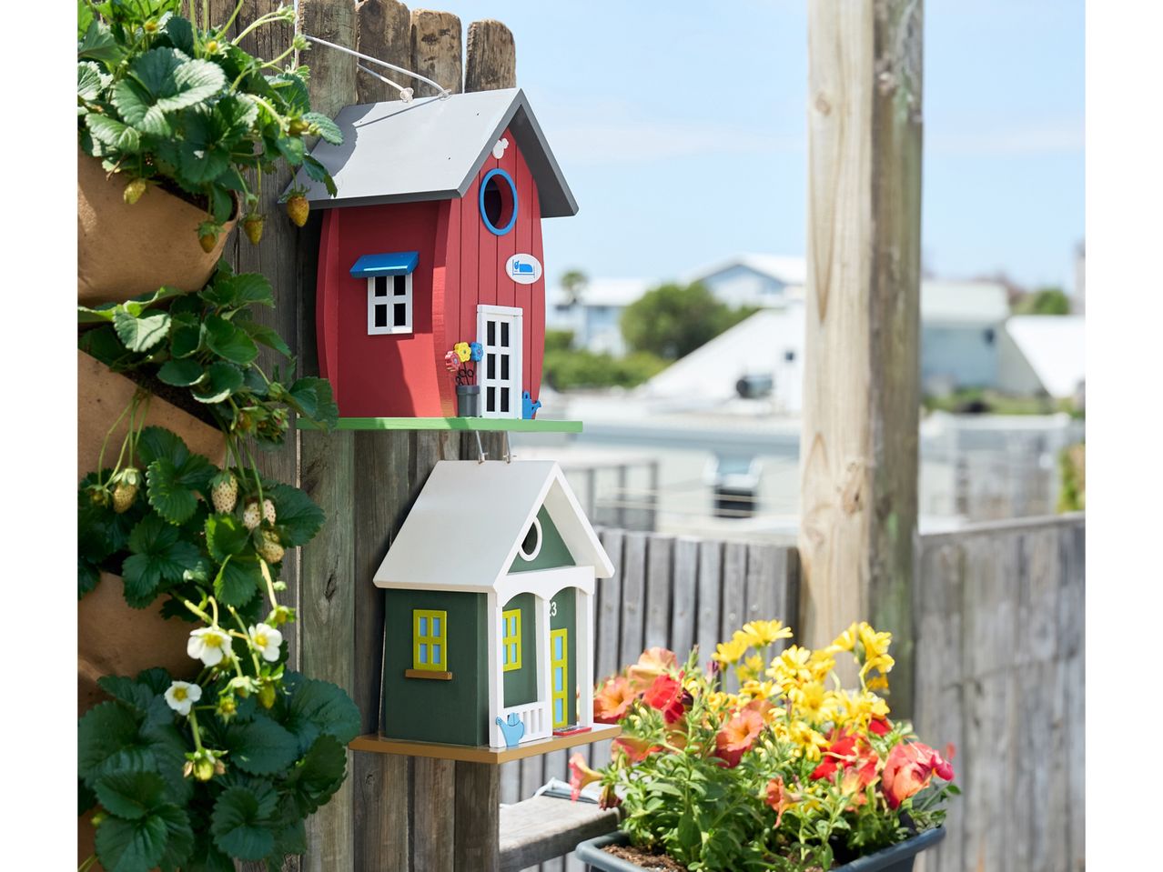 Two colorful birdhouses and a vertical strawberry planter on a wooden fence.