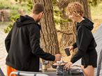 Two people preparing a meal outdoors, with camping gear and a tent nearby.