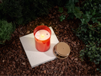 LIVARNO home LED-gravljus, lit red candle on a white slab, surrounded by bark and greenery.