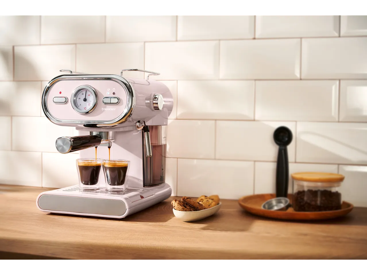 Pink SilverCrest espresso machine brewing coffee into two glasses on a wooden counter.