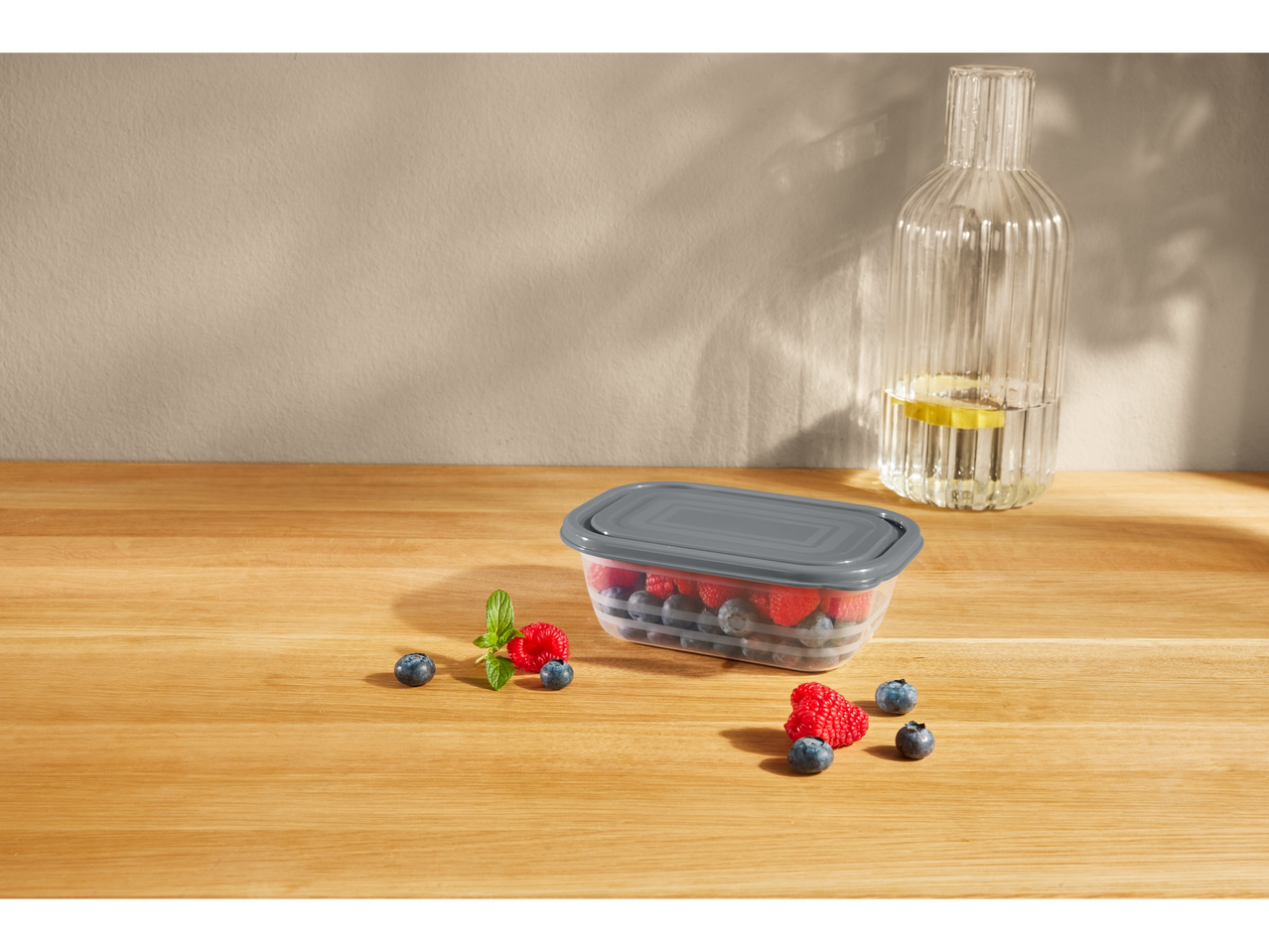 Gray plastic food container with raspberries and blueberries.