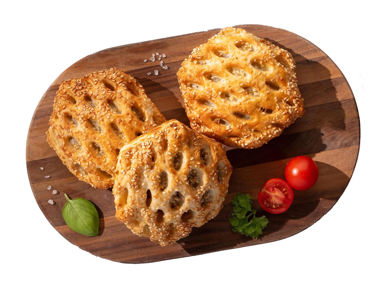 Három szezámmagos, rácsos leveles tészta paradicsommal és fűszernövényekkel egy fa tálalódeszkán.