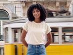 Woman in cream eyelet t-shirt and denim shorts, smiling in front of a moving tram.