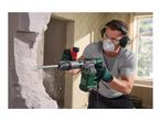 Man using a demolition hammer to break a wall, wearing safety gear.