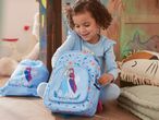 A toddler plays with a Frozen-themed backpack and drawstring bag.
