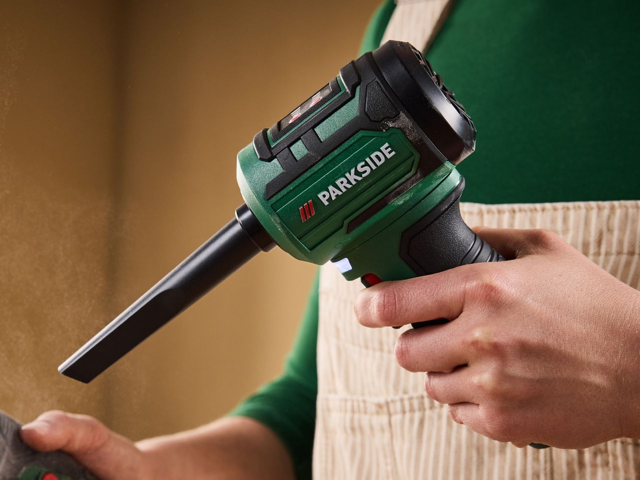 A person holding a green and black handheld power tool with a long nozzle.